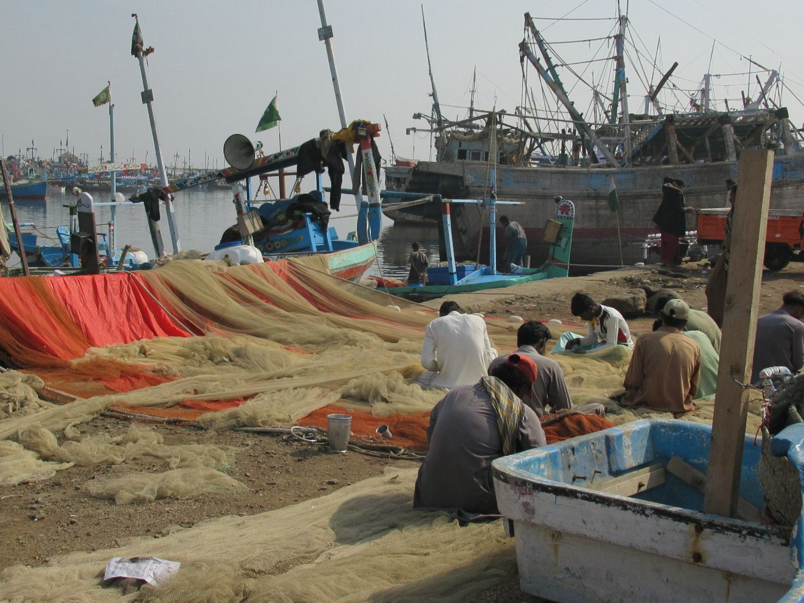 Fisherfolk mending nets beside moored boats at a harbour